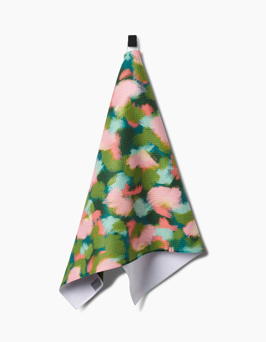 Geometry stroke of genius print tea towel with green, blue and pink colors hanging on a hook