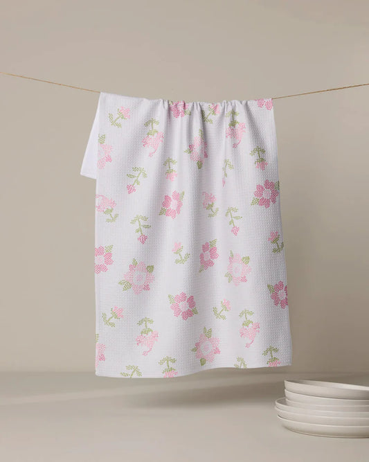 Geometry Cross Stitch Floral patterned towel hanging on a line against a beige wall.
