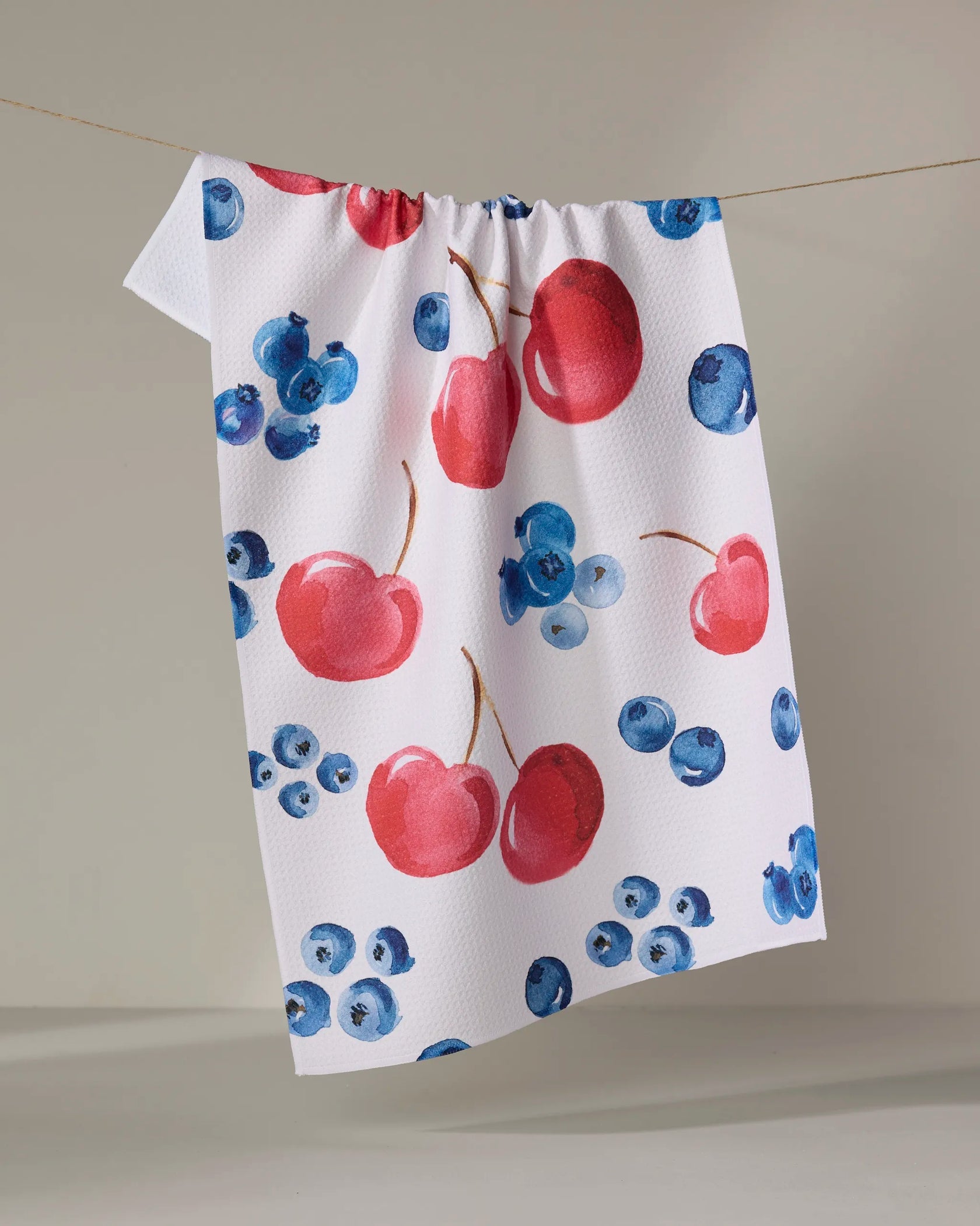 geometry=t Towel with red cherries and blueberries pattern hanging on a line.
