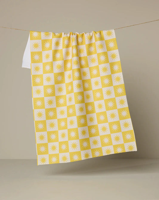 Yellow and white checkered Geometry Sundial tea towel with sun pattern hanging on a line against a beige background
