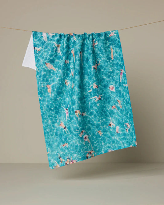 Geometry Swimming crowd Teal tea towel with pool scene pattern hanging on a line against a beige background
