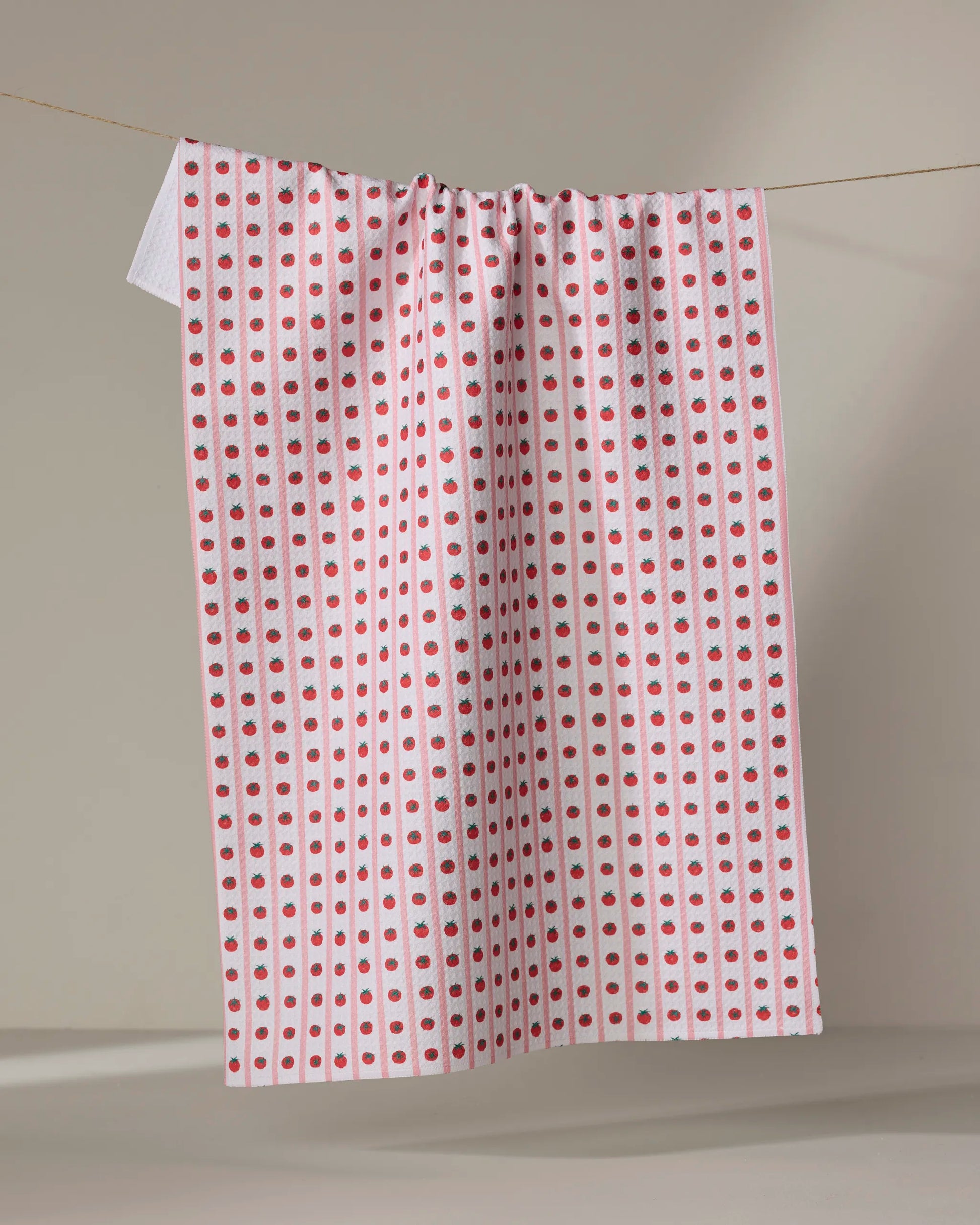 Highly absorbent and quick drying kitchen tea towel by Geometry made with Geoweave featuring the Tomato Stripes print with pink stripes and columns of red tomatoes.
