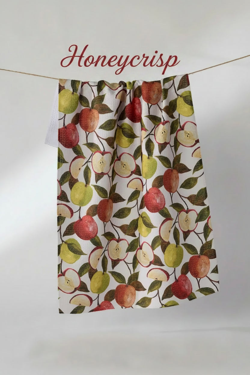 A geometry honeycrisp tea kitchen towel with a watercolor-style apple pattern, hanging from a string against a plain light gray background.