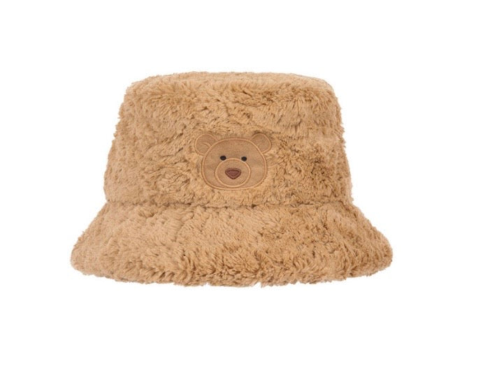 A plush teddy bear face bucket hat in a warm tan color, featuring a soft faux fur texture and a stitched bear face on the front, set against a plain white background.