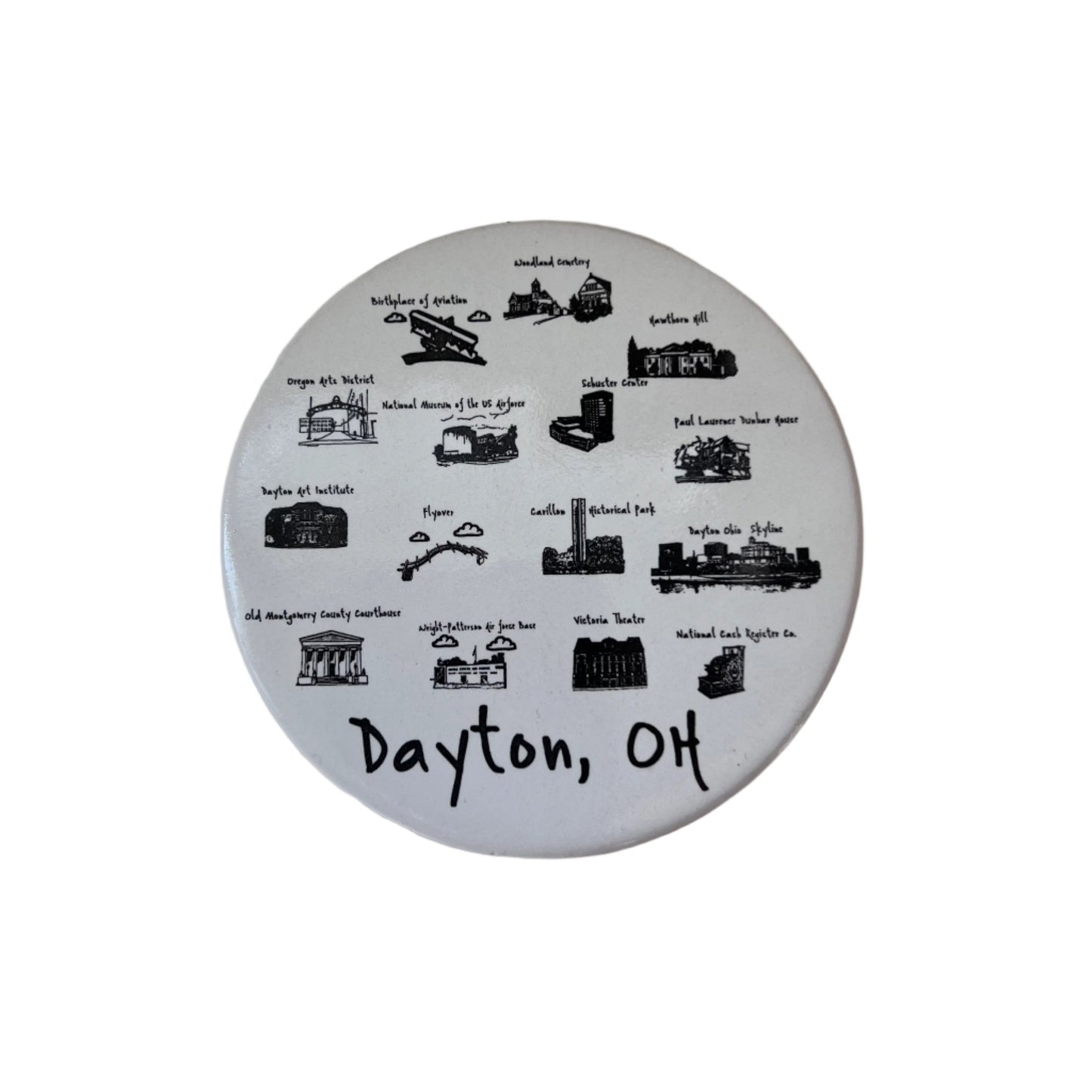 A round ceramic coaster with illustrations and text promoting Dayton, OH. It features iconic local imagery and is primarily white with black and gray details.