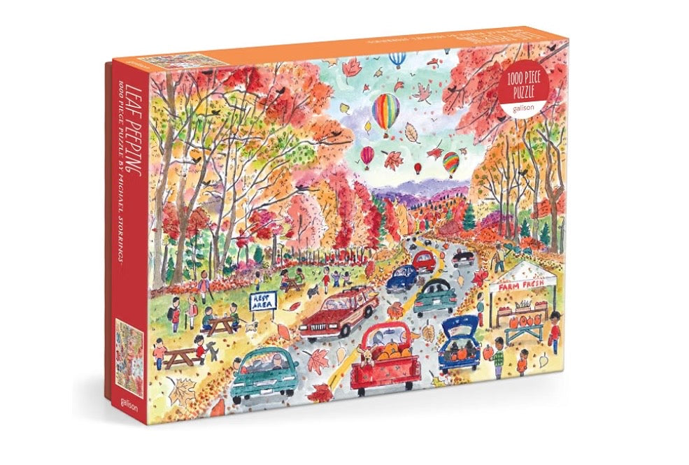 A 1000-piece jigsaw puzzle box titled 'Leaf Pecking' by artist Jane Fitch, featuring a colorful autumn scene with cars, people, hot air balloons, and fall foliage.
