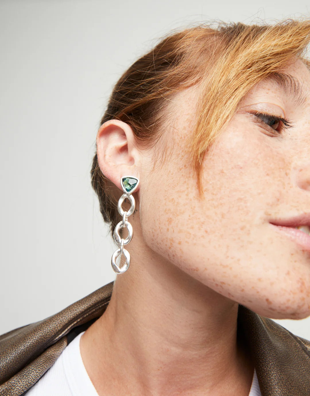 Woman wearing UNOdo50 silver and green dangle chain earrings.