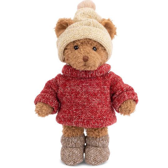 Teddy bear wearing a red sweater, beige hat, and brown boots on a white background