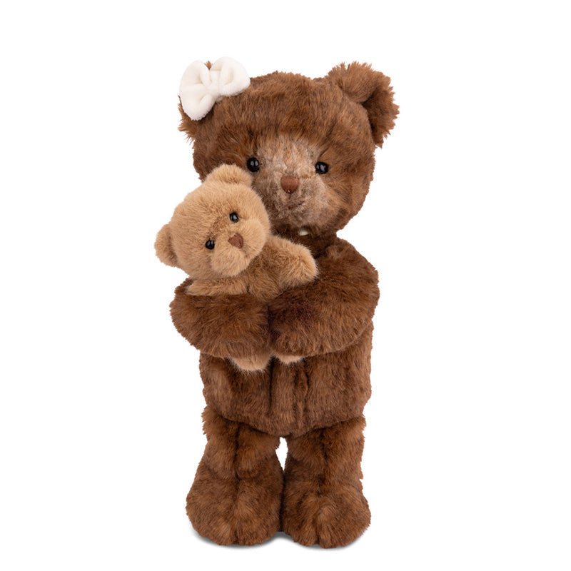 A brown plush teddy bear standing upright and holding a smaller tan teddy bear, with a white bow on its head, photographed against a plain white background.