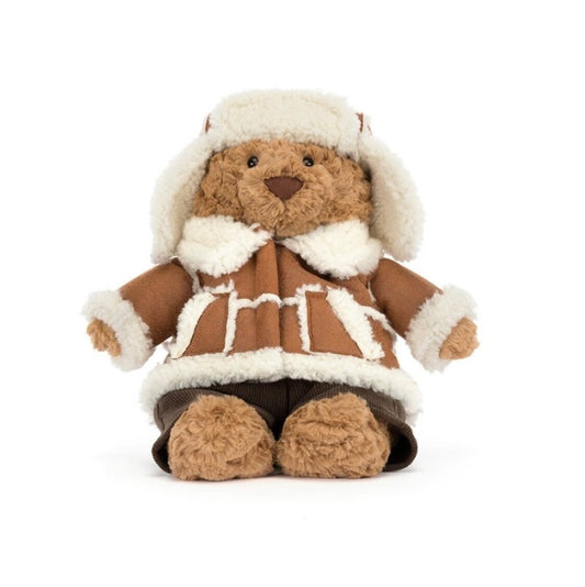 A plush teddy bear dressed in a brown and white faux-shearling winter outfit with a matching hood, photographed against a plain white background.
