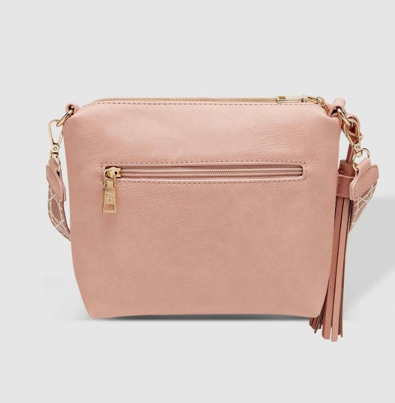 A blush pink Louenhide Kasey Crossbody Bag with a tassel, showcasing the front zipper pocket and the adjustable straps.