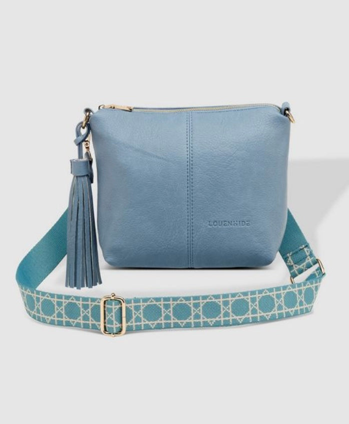 A blue Louenhide Kasey Crossbody Bag with a geometric patterned strap and a tassel detail on the zipper.