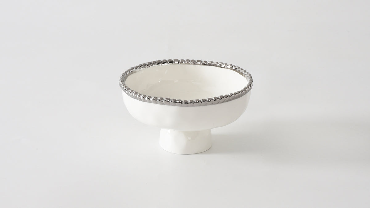 A small white porcelain footed bowl with silver beading around the rim.