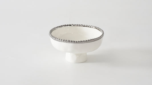 A small white porcelain footed bowl with silver beading around the rim.