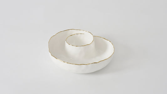 A white porcelain chip and dip serving dish with delicate gold trim on the edge and shaped like a shell.
