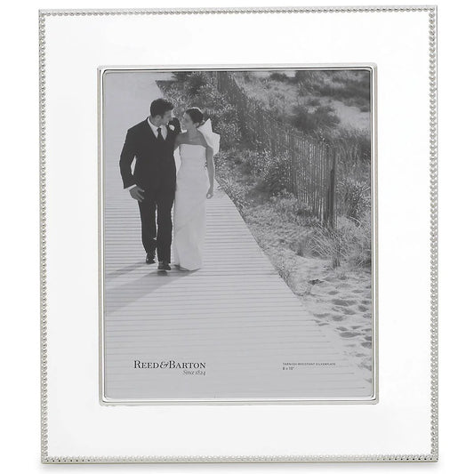 A silverplate picture frame with a beaded design, displaying a black and white photograph of a couple walking hand in hand on a boardwalk.