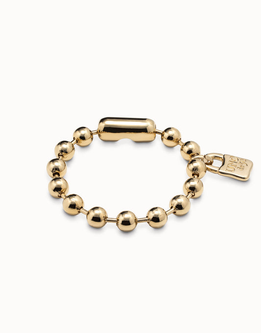 A gold-colored bracelet with a rounded pattern and a padlock UNOde50 charm, featuring small spherical decorations along the length.