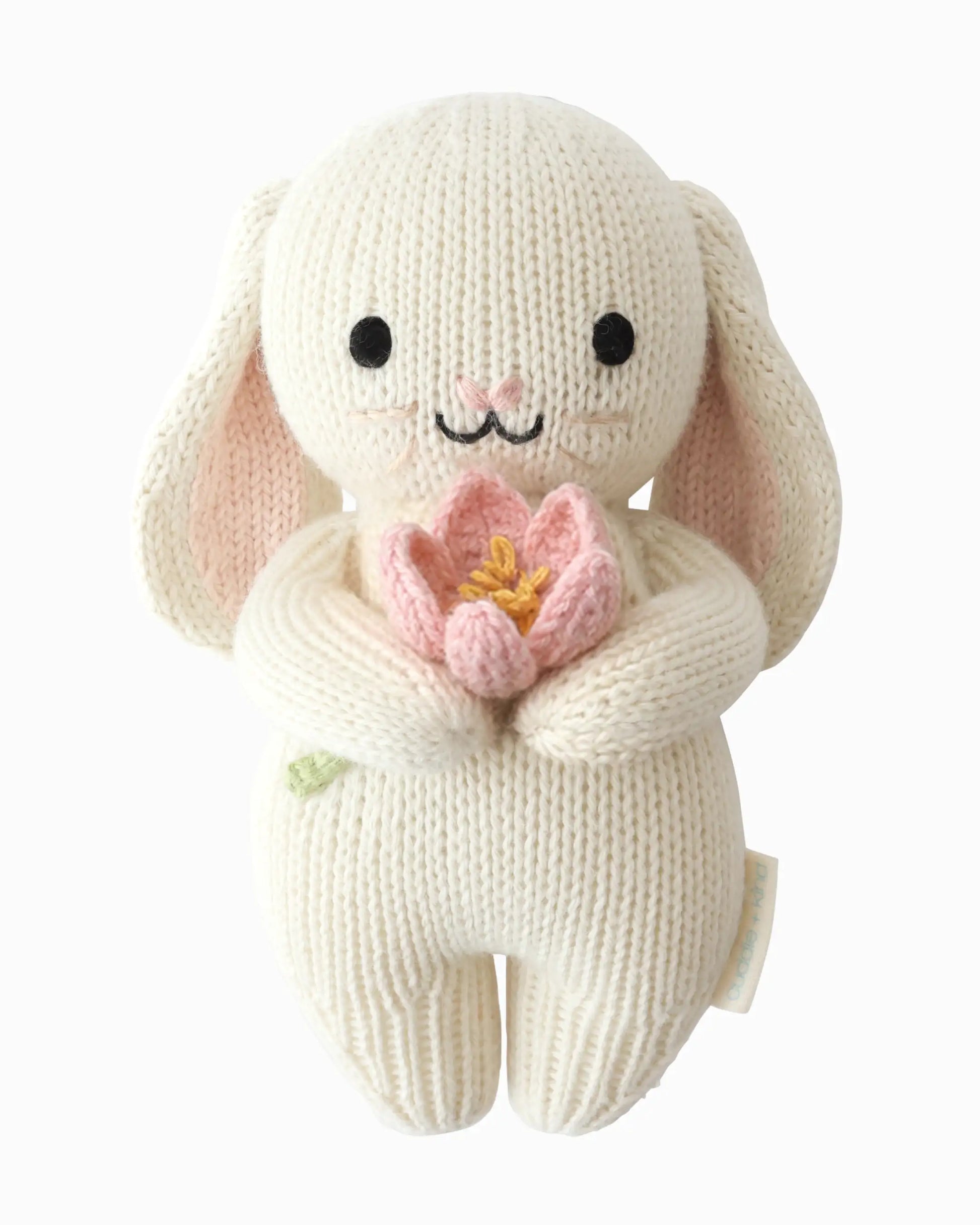 Knitted bunny toy holding a pink flower on a white background
