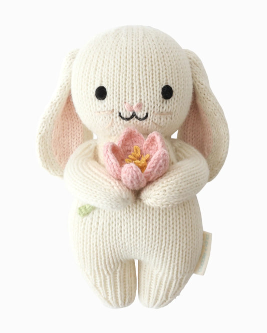 Knitted bunny toy holding a pink flower on a white background