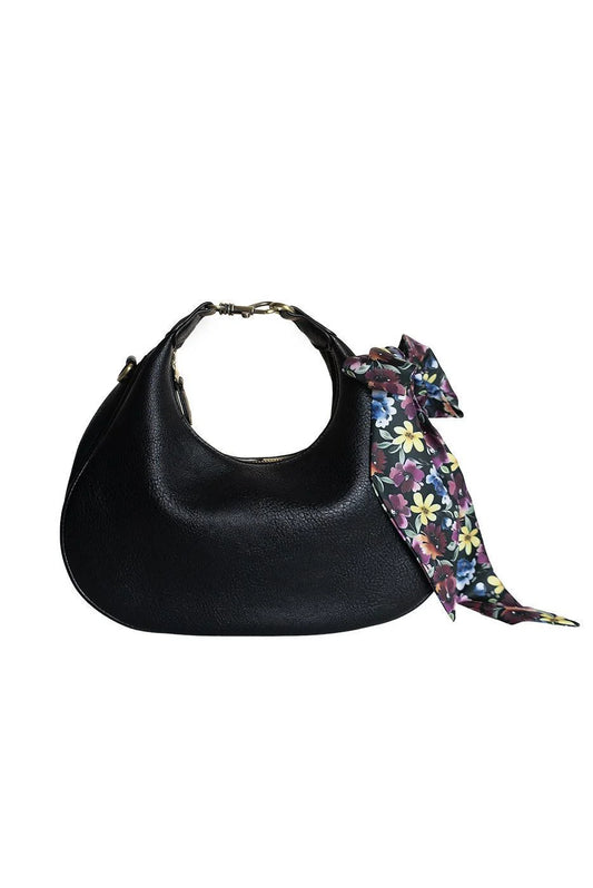 A black pebbled leather crescent-shaped shoulder bag with a colorful floral silk scarf tied in a bow around the strap, shown against a plain white background.