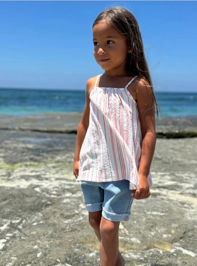 Young girl standing on a beach wearing a Vignette Mallory Tank Top with Red Stripes with ocean in the background