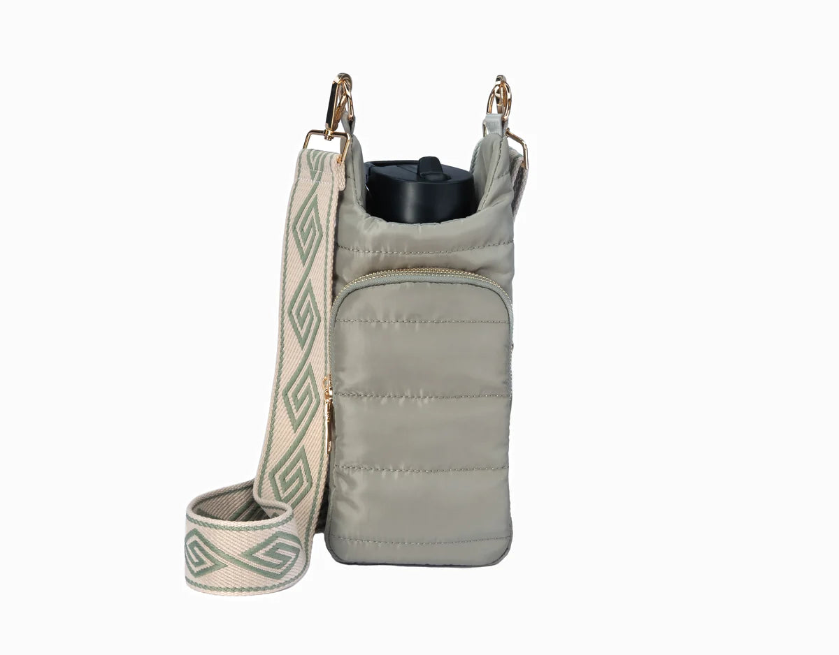 A sage green water bottle bag with a quilted fabric and a strap, designed to keep a water bottle secure while carrying other essentials in the pockets.