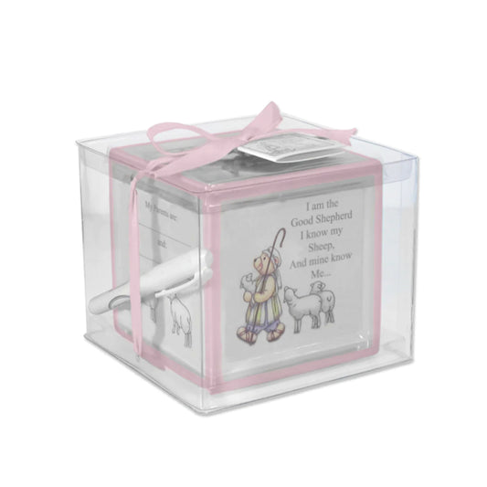 A ceramic block bank designed with pink colorful borders, intended for recording christening moments, shown with a ribbon and tag.