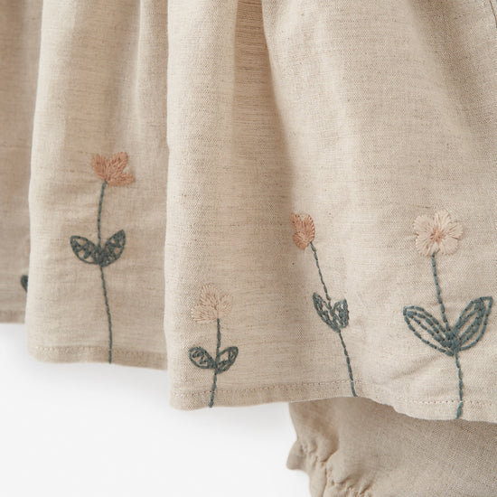 Close-up of beige fabric with embroidered flowers on a baby dress on a white background