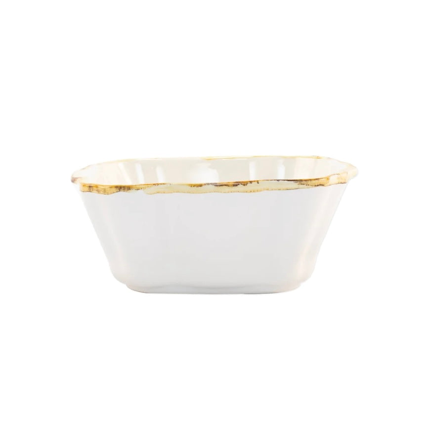 A small square white ceramic baker with scalloped edges and a rustic brown rim.