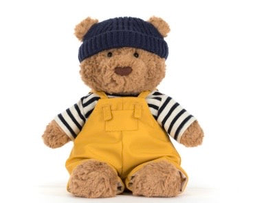 Teddy bear wearing a navy hat and yellow overalls on a white background