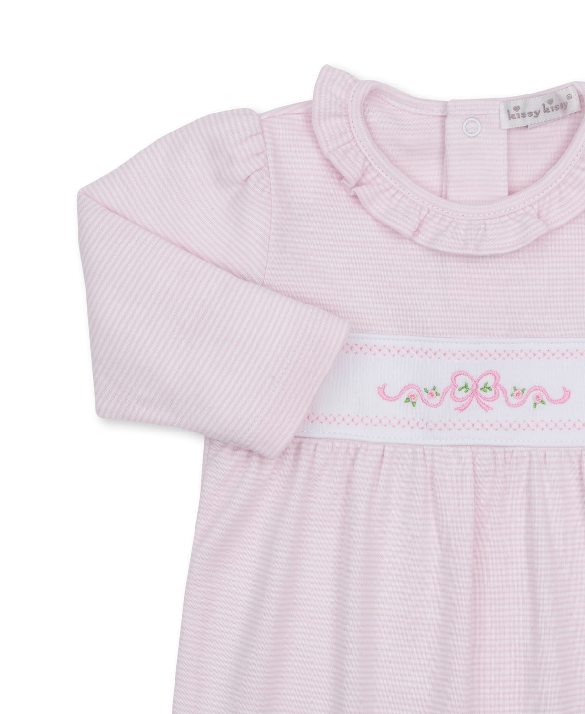 A close-up of a baby girl's long-sleeve Kissy Kissy Classic Treasures footie, featuring light pink and white horizontal stripes, a ruffled collar, and a smocked waistband with pink bows and green floral details.