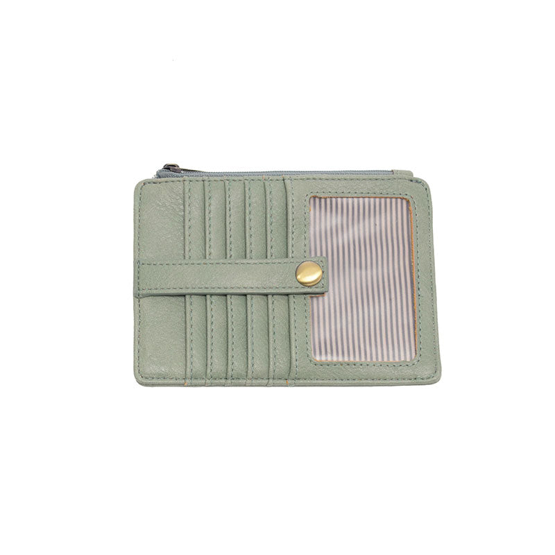 A dusty sage green mini travel wallet made of vegan leather, featuring a top zip closure and multiple card slots, with a brass plated hardware button.