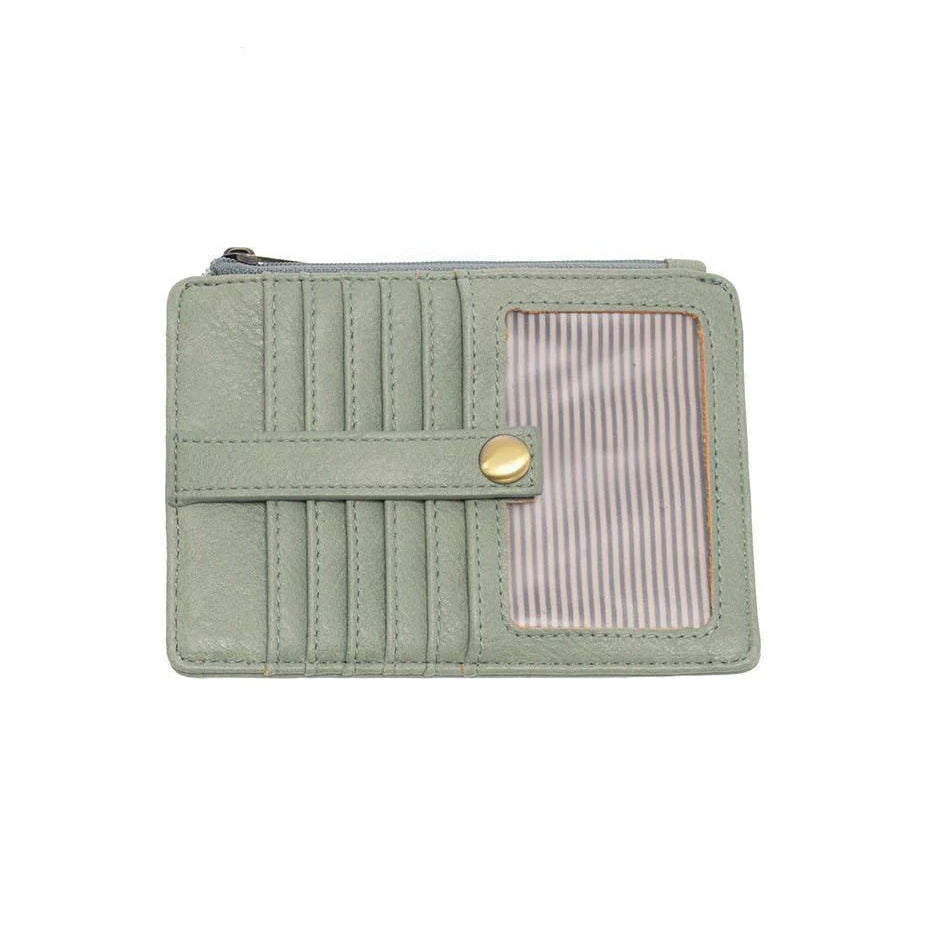 A dusty sage vegan leather mini travel wallet with a top zip closure, multiple card pockets, an ID window pocket, and an exterior passport pocket. It has brass plated hardware and is slim enough for travel use.