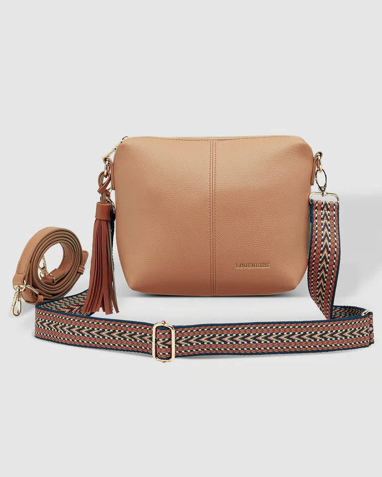 Ablush  pebbled leather crossbody louenhide  bag with a matching tassel and a wide woven patterned shoulder strap, displayed on a light gray background.