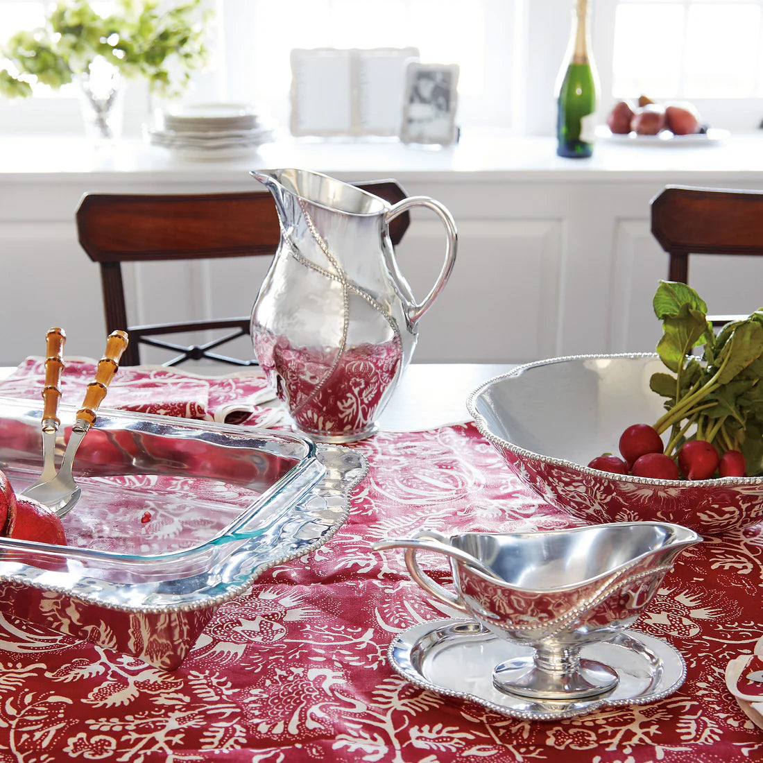 Dining table set with silverware and glassware from the Mariposa Sueño  Collection and a red patterned tablecloth.