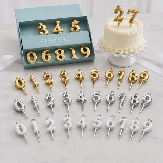 Mariposa gold and silver number candle toppers displayed on a light marble surface, with their blue presentation box and a decorated cake topper example shown.