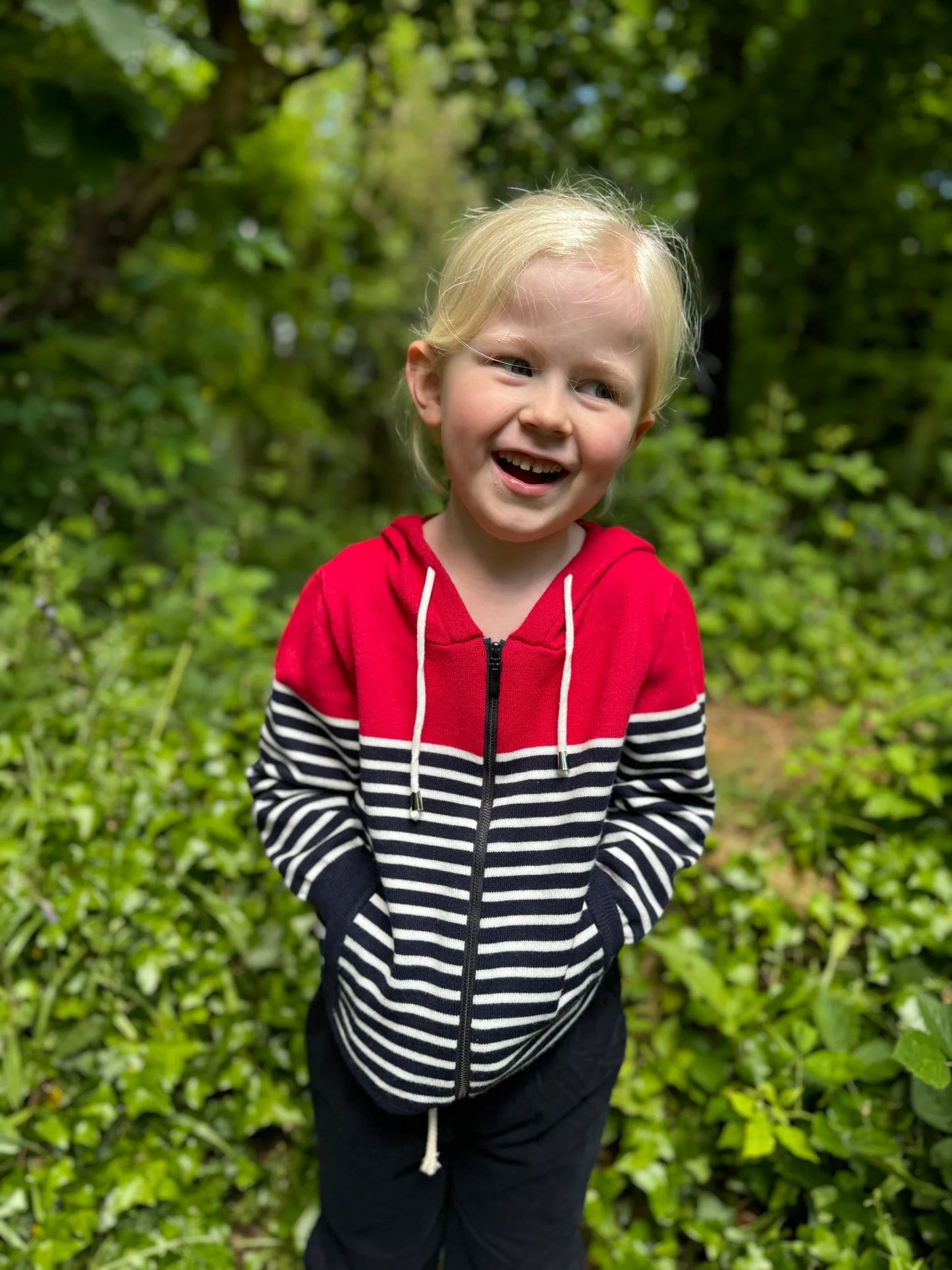 Child wearing a Me and Henry Sagamore Red/White Stripe Zip Up Hoodie standing in a green outdoor setting