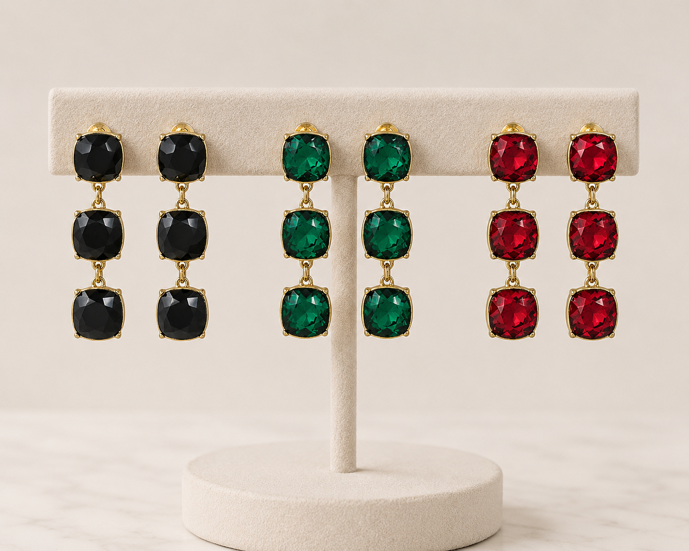 Meghan Browne PRYN-RU PRYN-EM PRYN-BD triple stone dangle earrings in black ruby and emerald on a display rack