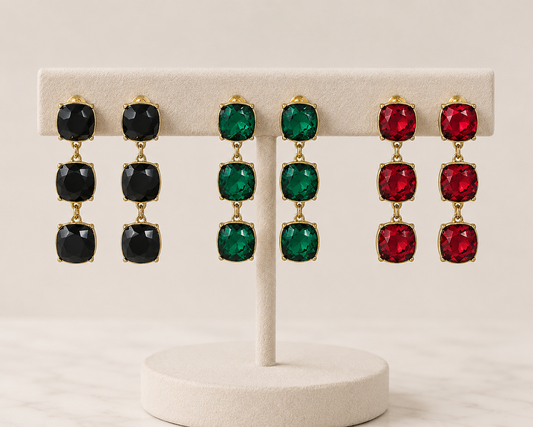 Meghan Browne PRYN-RU PRYN-EM PRYN-BD triple stone dangle earrings in black ruby and emerald on a display rack