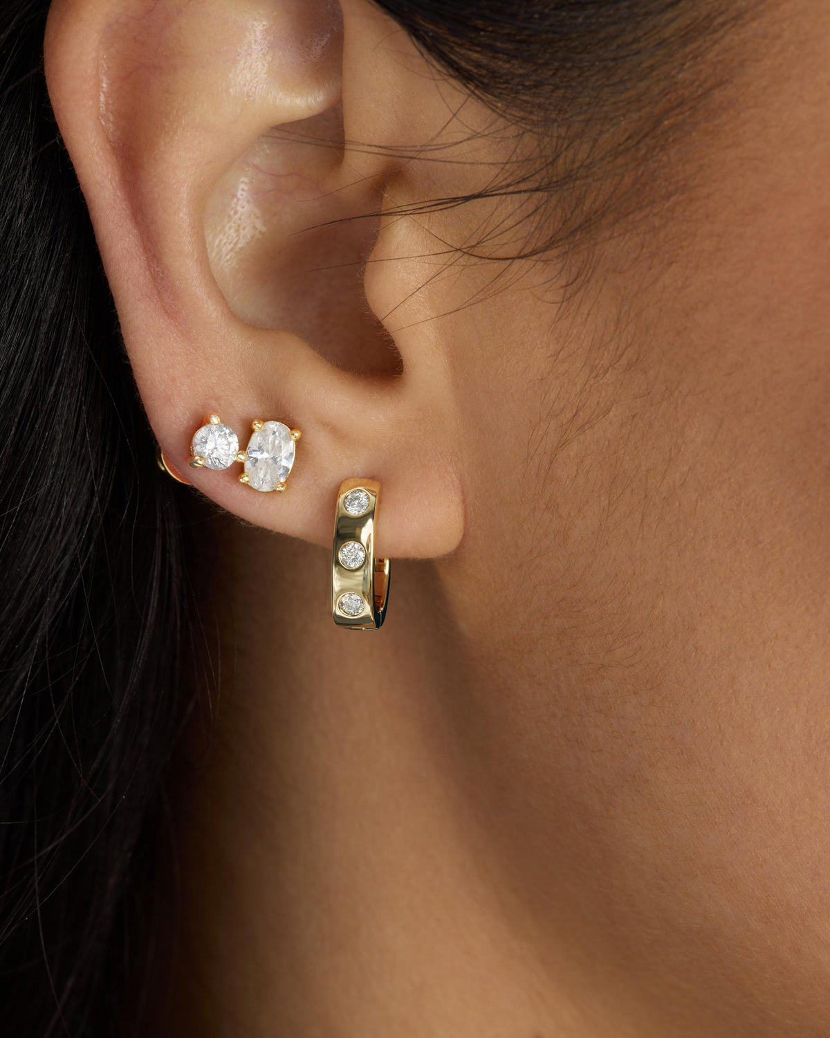 Close-up of an ear wearing Melinda Maria gold hoop Ashley earrings with clear gemstones.