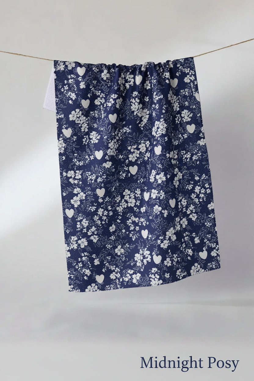 A navy blue Geometry midnight posy tea towel with a white floral and heart pattern, hanging from a thin wire against a plain light gray studio background.