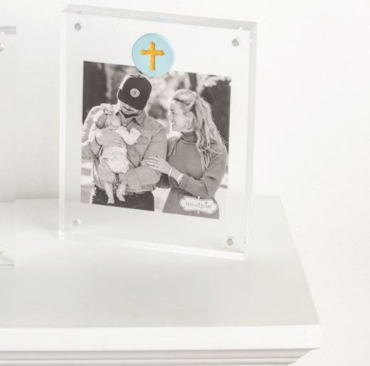 Picture of the Mudpie acrylic picture frame displayed on a table with a blue circle with a cross.