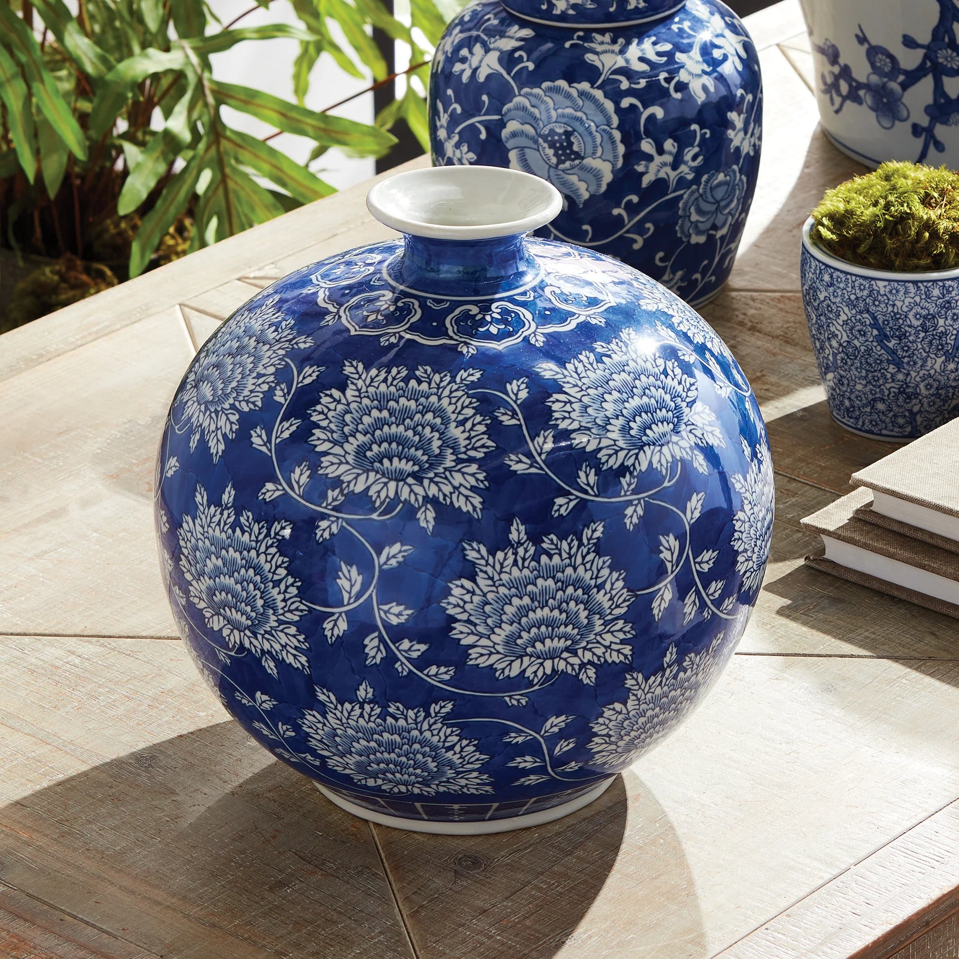 Blue and white floral-patterned vase on a wooden surface with plants in the background