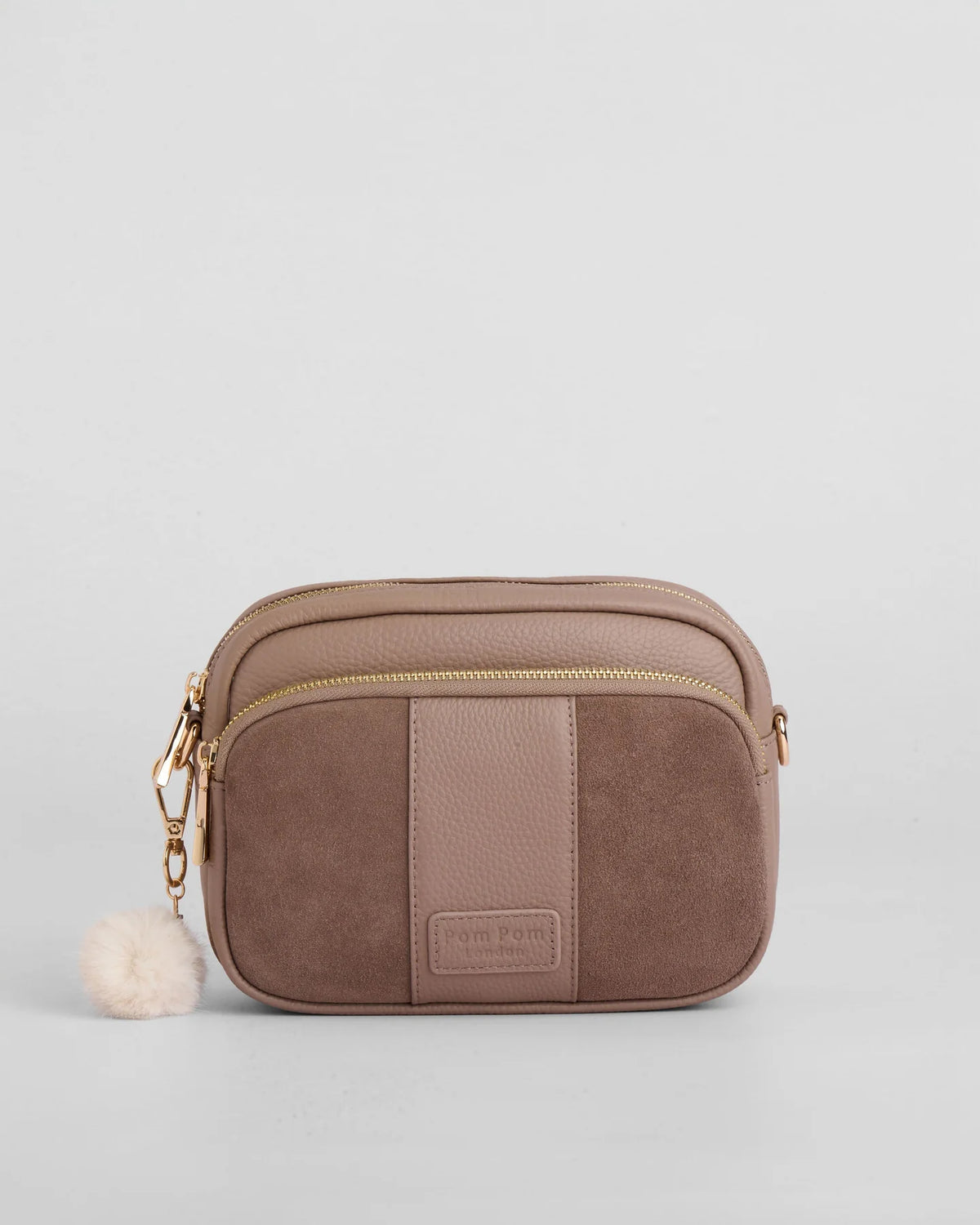Mocha suede crossbody bag with gold zipper and pom pom tassel on a light gray background