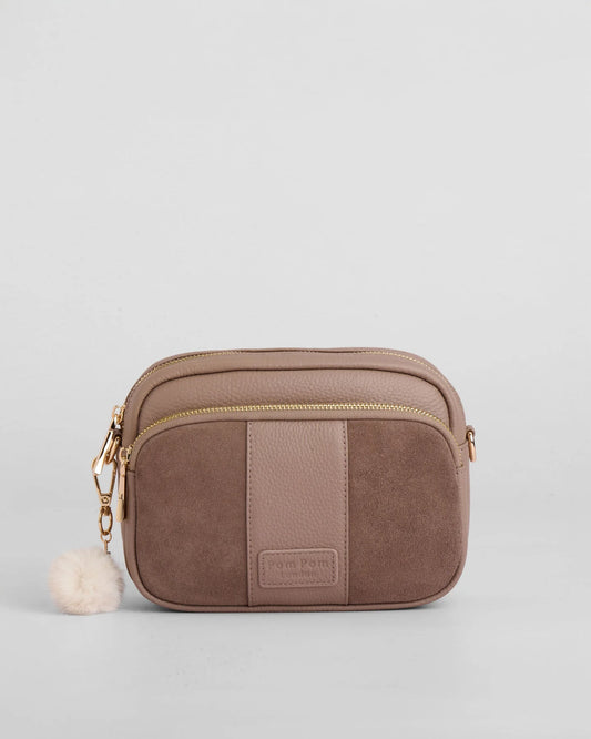 Mocha suede crossbody bag with gold zipper and pom pom tassel on a light gray background