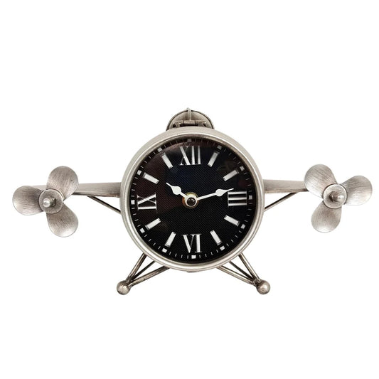 A metal decorative airplane-shaped table clock with a black face, white Roman numerals, and silver metallic propeller wings and body.