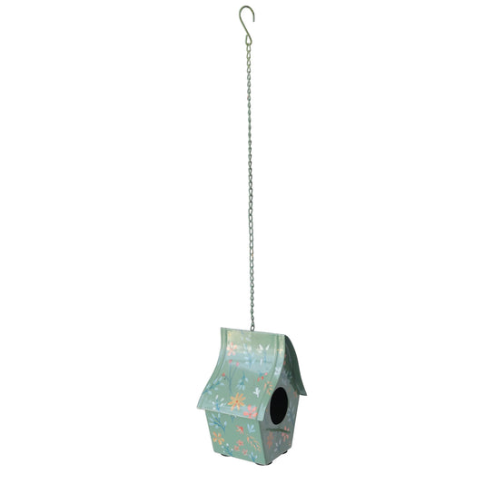 A hanging birdhouse with a light background with a floral pattern, suspended by a silver metal chain from a hook. 