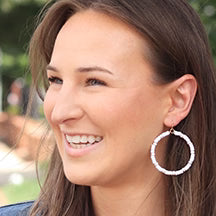 Woman wearing Pierce & HIde rubber hoop earrings with a blurred outdoor background