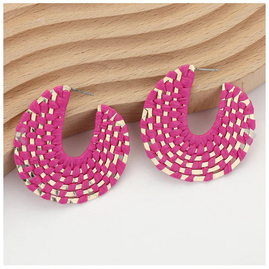 Pierce and Hide Pink and gold woven hoop earrings on a wooden surface