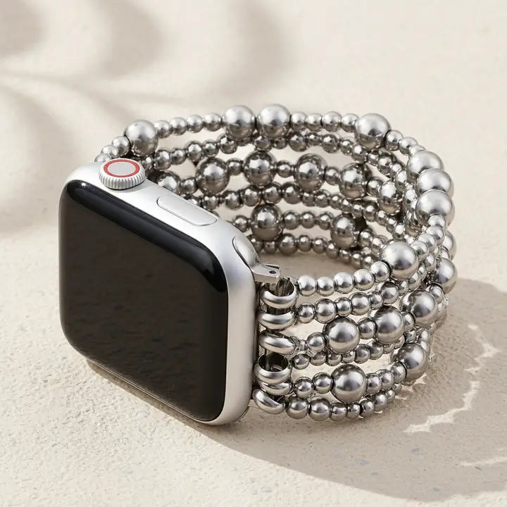 Platinum demure stretch apple watch strap by cape diablo with a silver beaded band on a beige surface